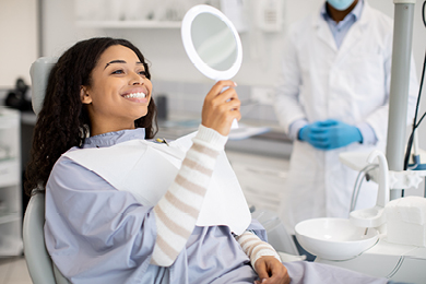 woman looking at her teeth in the mirror at the dentist's office